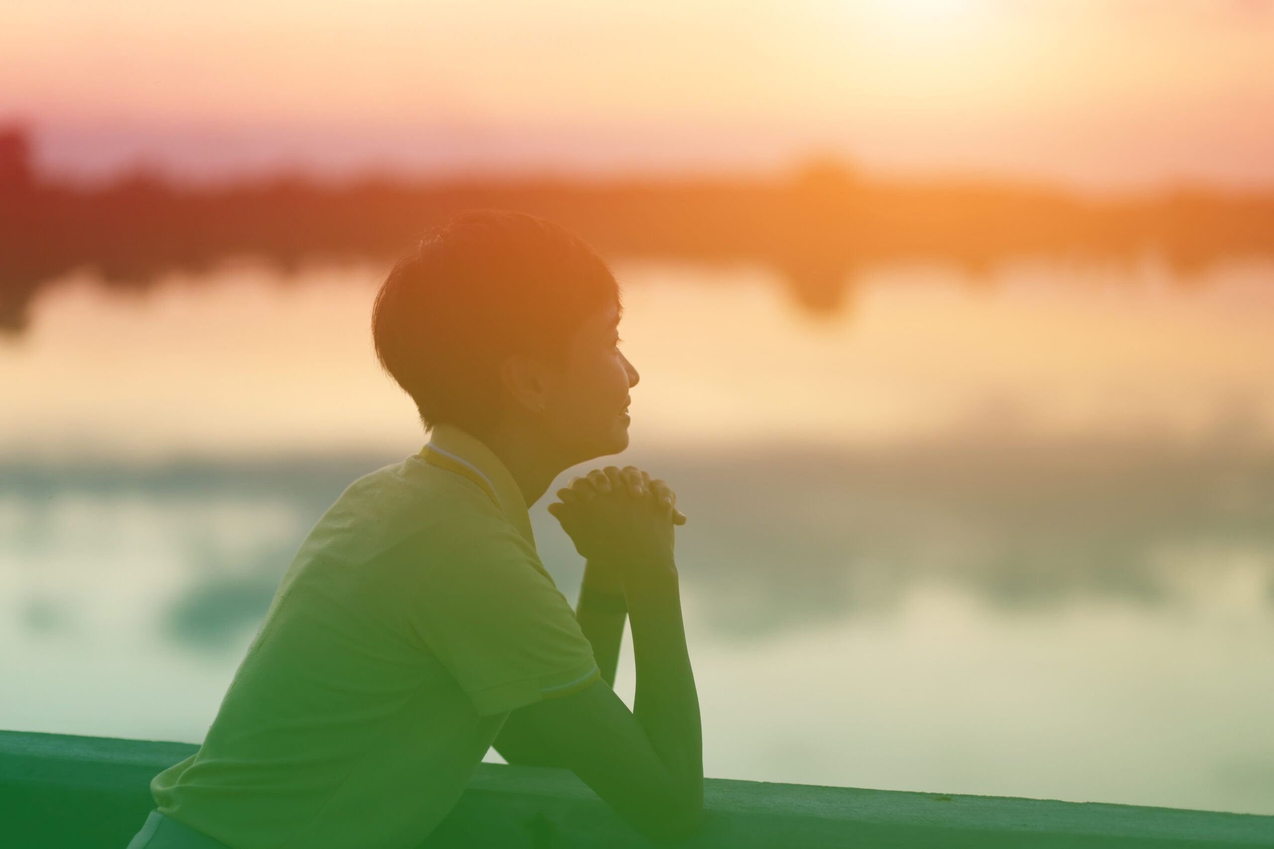 Person sitting by the water at sunset, reflecting quietly on mental health and emotional well-being